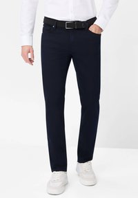 Pantalones azul marino de algodón, con un diseño de pierna recta. Combinados con un cinturón trenzado negro texturizado y zapatillas deportivas blancas.