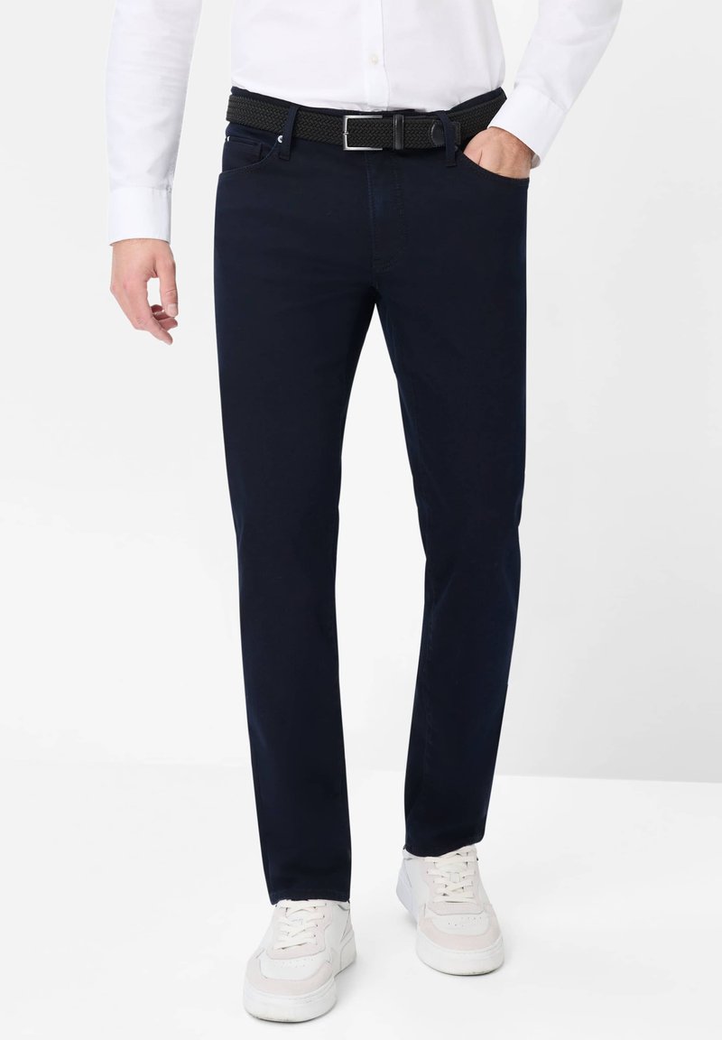 Pantalones azul marino de algodón, con un diseño de pierna recta. Combinados con un cinturón trenzado negro texturizado y zapatillas deportivas blancas.