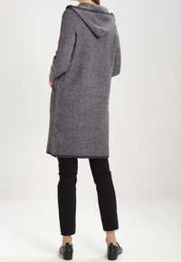 Abrigo gris de patrón de espiga con capucha, de corte recto y mangas largas, usado sobre pantalones y zapatos negros.