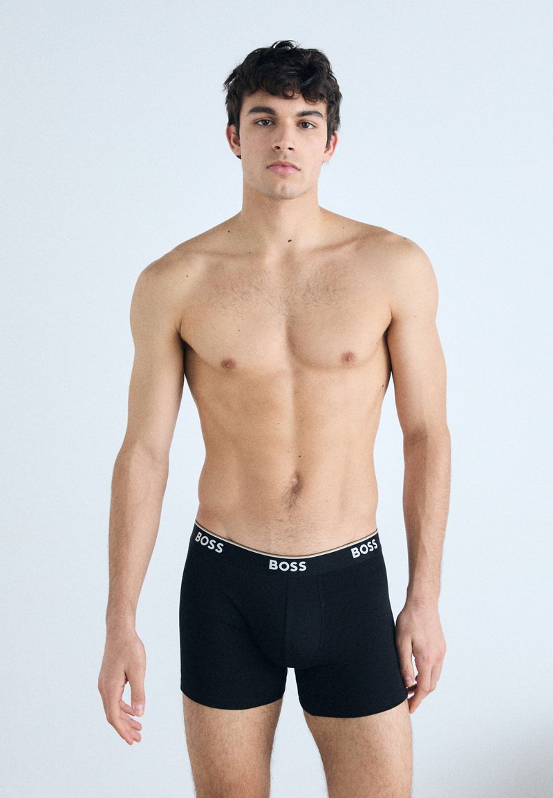 Schwarze Boxershorts mit einem weißen "BOSS"-Logo am Bund. Der Stoff wirkt glatt und eng anliegend, entworfen für Komfort und Unterstützung.
