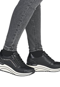 Zwarte sneakers met een textuur aan de zijkant, vetersluiting, een zijrits en een witte, gebogen zool; gedragen met slim fit grijze jeans.