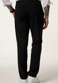 Mustat housut, joissa on kuvioitu pinta, joustava vyötärö ja sivutaskut. Näkyvät saumat ja räätälöity istuvuus lahkeissa.