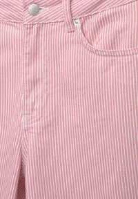 Tissu en denim rayé verticalement rose et blanc avec un bouton métallique, un rivet, une boucle de ceinture et des coutures de poche en gros plan.