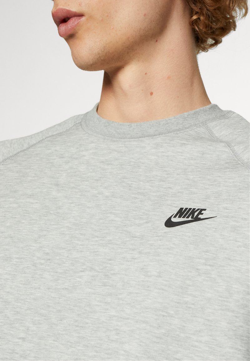 Sweat-shirt gris avec un col rond, des manches raglan, et un logo Nike noir sur la poitrine. Le matériau semble doux et texturé.