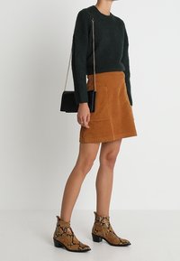 Zelený chlupatý pletený svetr, oranžová kordurová mini sukně, černá kabelka a hnědé hadí kožené kotníkové boty na blokovém podpatku.