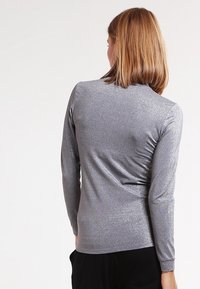 Pitkähihaista paitaa kiiltävässä hopeakankaassa, jossa on sileä rakenne ja istuva muotoilu, taakse kootun yksityiskohdan kanssa.