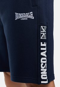 Mornarske plave kratke hlače od mekog materijala, s bijelim vezom "LONSDALE" logotipa i britanske zastave na boku. Standardni kroj, do koljena.