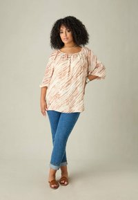 Top leggero in crema con righe ruggine, scollatura a barchetta, maniche 3/4. Abbinato a jeans skinny blu e sandali marroni. Texture liscia.