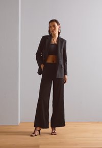 Svart skreddersydd blazer over en svart crop top og vide bukser, med teksturert stoff og høye sandaletter.
