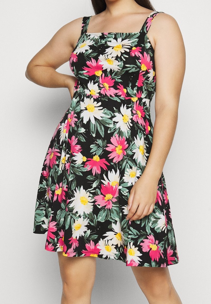 Sort blomsterkjole med hvide og lyserøde tusindfryd, med tætsiddende overdel, A-formet nederdel og tynde skulderstropper.