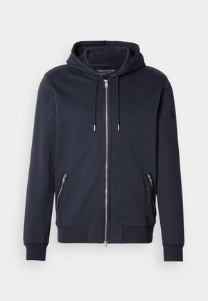 Navy Zip-Hoodie mit Zugkapuze, ausgestattet mit zwei seitlichen Reißverschlusstaschen und gerippten Bündchen. Hergestellt aus weichem, strukturiertem Stoff.