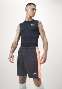 Fekete ujjatlan felső Under Armour logóval és sötétszürke rövidnadrággal, amely őszibarack színű akcentussal rendelkezik. Simább anyag és rugalmas derékszíj.