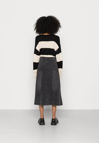 Zwart-wit gestreepte trui met lange mouwen, gecombineerd met een donkergrijze denim midi-rok en zwarte chunky schoenen, gezien vanuit de achterkant.