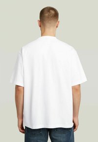 T-shirt bianco in cotone con vestibilità rilassata, maniche corte e scollo rotondo classico. Tessuto liscio, senza motivi o dettagli visibili.