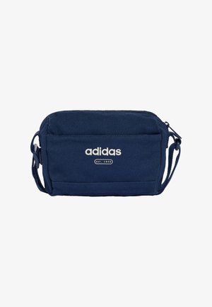 Granatowa mała torba na ramię Adidas z przednią kieszenią, białym logo, zamkiem błyskawicznym i regulowanym paskiem.