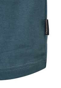 Teal cotton T-shirt with a smooth texture, featuring a small black label on the side seam and contrasting stitching at the hem.