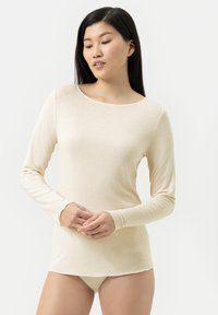 Haut beige clair à manches longues en tissu doux avec un col rond et une coupe ajustée, associé à un bas beige assorti.