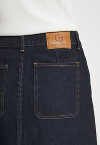 Mörka denimjeans med en brun läderlogotyp på baksidan, kontraststygn och två bakfickor med en klassisk passform.