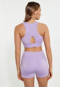 Lilla sport-bh med racerback-design og en nøglehul-cutout. Sammen med matchende lilla shorts med høj talje og glat tekstur.