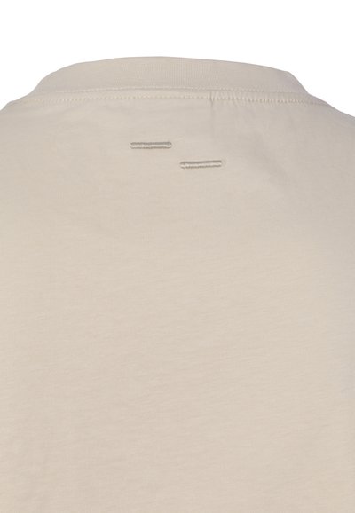 Beige Stoff mit Rundhalsausschnitt und zwei kleinen horizontalen Steppnähten nahe der oberen Rückenmitte, minimalistisches Designdetail.