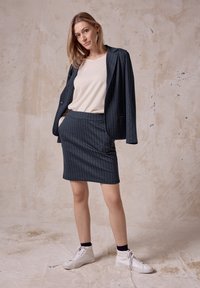 Marineblaues Nadelstreifen-Blazer- und Rock-Set aus strukturiertem Stoff, kombiniert mit einem hellen Oberteil und weißen High-Top-Sneakers.