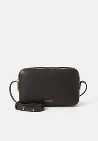 Černé kožené psaníčko se zipem v zlaté barvě, logem na přední straně, odnímatelným popruhem, obdélníkového tvaru, hladkou texturou, bez viditelných vzorů.