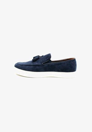 Chaussure slip-on en daim bleu marine avec une semelle en caoutchouc blanc, dotée d'un gland décoratif à l'avant et d'un doublure intérieure lisse.