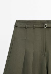 Jupe taille haute vert olive avec passants pour ceinture, ceinture assortie en tissu avec boucle métallique et détails plissés à l'avant.