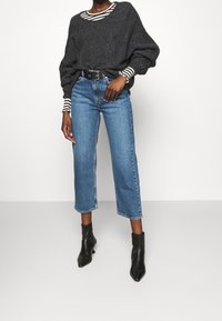 Oversized mörkgrå stickad tröja över en randig långärmad skjorta, kombinerat med korta blå jeans och spetsiga svarta ankelstövlar.