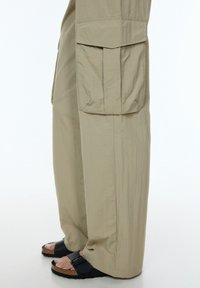 Beige, losse cargo pants van lichtgewicht stof, met grote zijzakken en een rechte snit, gedragen met zwarte sandalen.