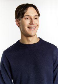 Maglione girocollo blu navy con un collo a coste. La trama lavorata a maglia è visibile; il tessuto appare morbido e aderente sulle spalle.
