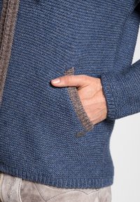 Gebreide jas in donkerblauw met een gestructureerde afwerking. Heeft een bruine rand langs de rits en een zijzak. Zachte stof, casual ontwerp.