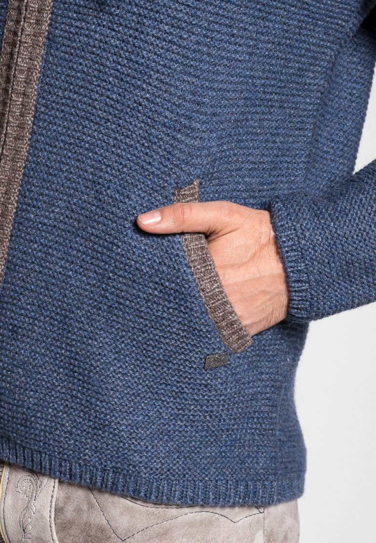 Gebreide jas in donkerblauw met een gestructureerde afwerking. Heeft een bruine rand langs de rits en een zijzak. Zachte stof, casual ontwerp.