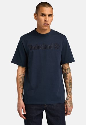 Navy blue cotton t-shirt with embossed "Timberland" logo and tree emblem on the chest. Standard fit with short sleeves and crew neck.
