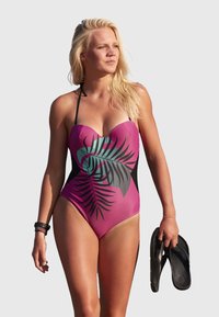 Maillot de bain une pièce rose avec un motif de feuilles de palmier noir et turquoise. Présente un décolleté en cœur et des bretelles ajustables.