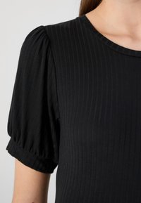 Top negru cu dungi, cu mâneci scurte și puffate și decolteu rotund. Materialul are o textură netedă și o croială strânsă, punând accent pe o siluetă elegantă.