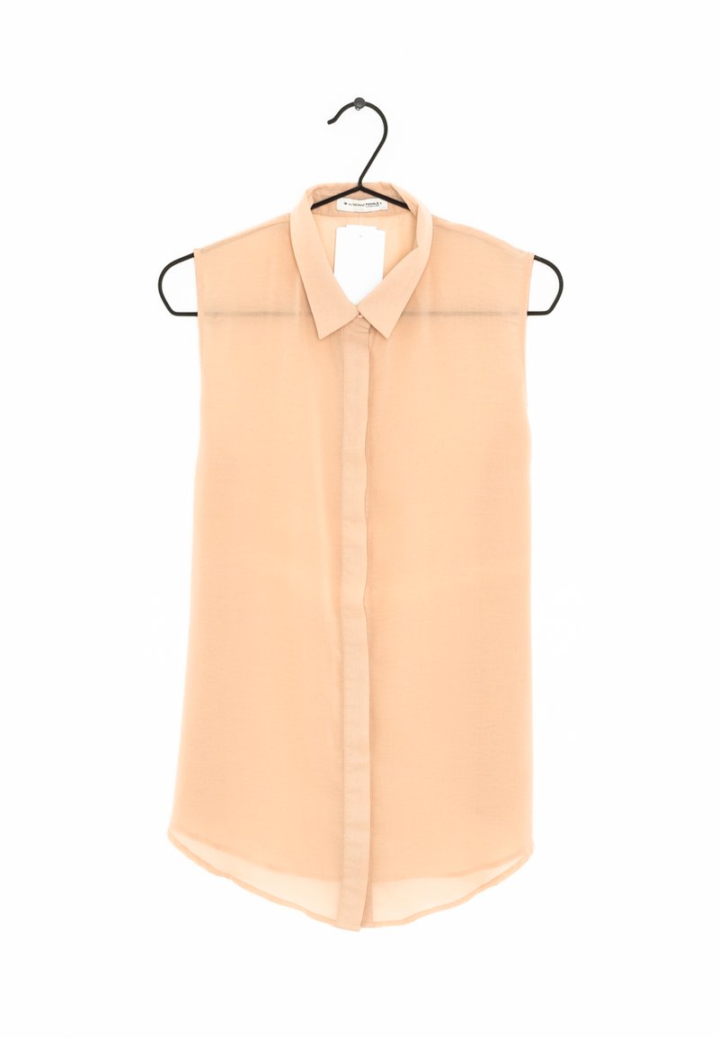Blouse sans manches pêche avec un col, patte de boutonnage, tissu transparent et ourlet arrondi. Suspendue à un cintre noir.
