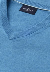 Jasnoniebieski sweter z dekoltem w serek, ze ściągaczem przy kołnierzu i czarną metką marki Hackett London wszytą wewnątrz przy szyi.