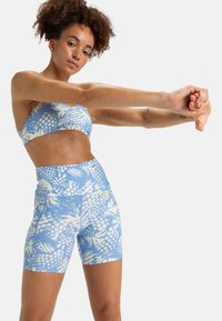 Ensemble de sport comprenant un soutien-gorge et un short à motif bleu, fabriqué dans un matériau extensible, présentant un design floral en blanc. Texture lisse, forme ajustée.