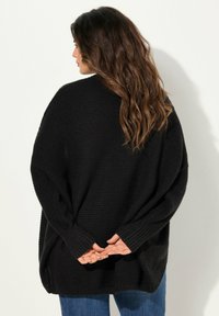 Svart oversized stickad tröja med långa ärmar, texturerad tyg och ribbade muddar, bärs över blå denimjeans.