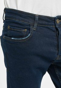 Tummansiniset farkut slim fit -mallissa, joissa on oranssia ommelta, etutasku ja kevyttä kulutusta reunoissa.