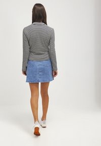 Zwart-wit gestreept longsleeve shirt gecombineerd met een lichtblauwe denim rok met een uitlopende zoom en twee achterzakken. Witte sneakers.
