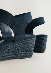 Tamno plave wedge sandale s teksturiranim gornjim dijelom od tkanine i elastičnim trakama, koje imaju tkani jutu srednji potplat i tamnu gumenu potplat.