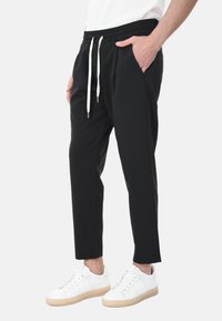 Pantaloni jogger neri con vita elasticizzata e cordini, tasche laterali e design a gamba affusolata, abbinati a sneakers bianche.