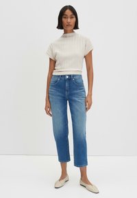 Beige geribbelde top met korte omgeslagen mouwen, gecombineerd met lichtblauwe cropped jeans en crèmekleurige platte schoenen. Eenvoudig, modern ontwerp.