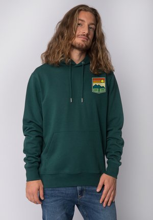 Hoodie vert en tissu doux, doté d'une poche frontale, d'une capuche avec cordon de serrage et d'un logo graphique coloré avec des montagnes et la phrase "GOOD VIBE."