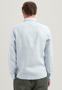 Camisa de manga larga azul claro hecha de lino, con un cuello clásico, puños abotonados, yugo trasero, y un acabado suave y texturizado.