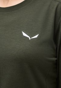 Πουκάμισο από σκουρόχρωμο χακί ριμπ ύφασμα με μικρό λευκό γωνιακό λογότυπο στο κέντρο του στήθους.