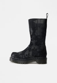 Melnas pusgarās zābaki ar kamuflāžas rakstu, bieza rievota zole, noapaļots pirksts un cilpa aizmugurē uz baltas fona.