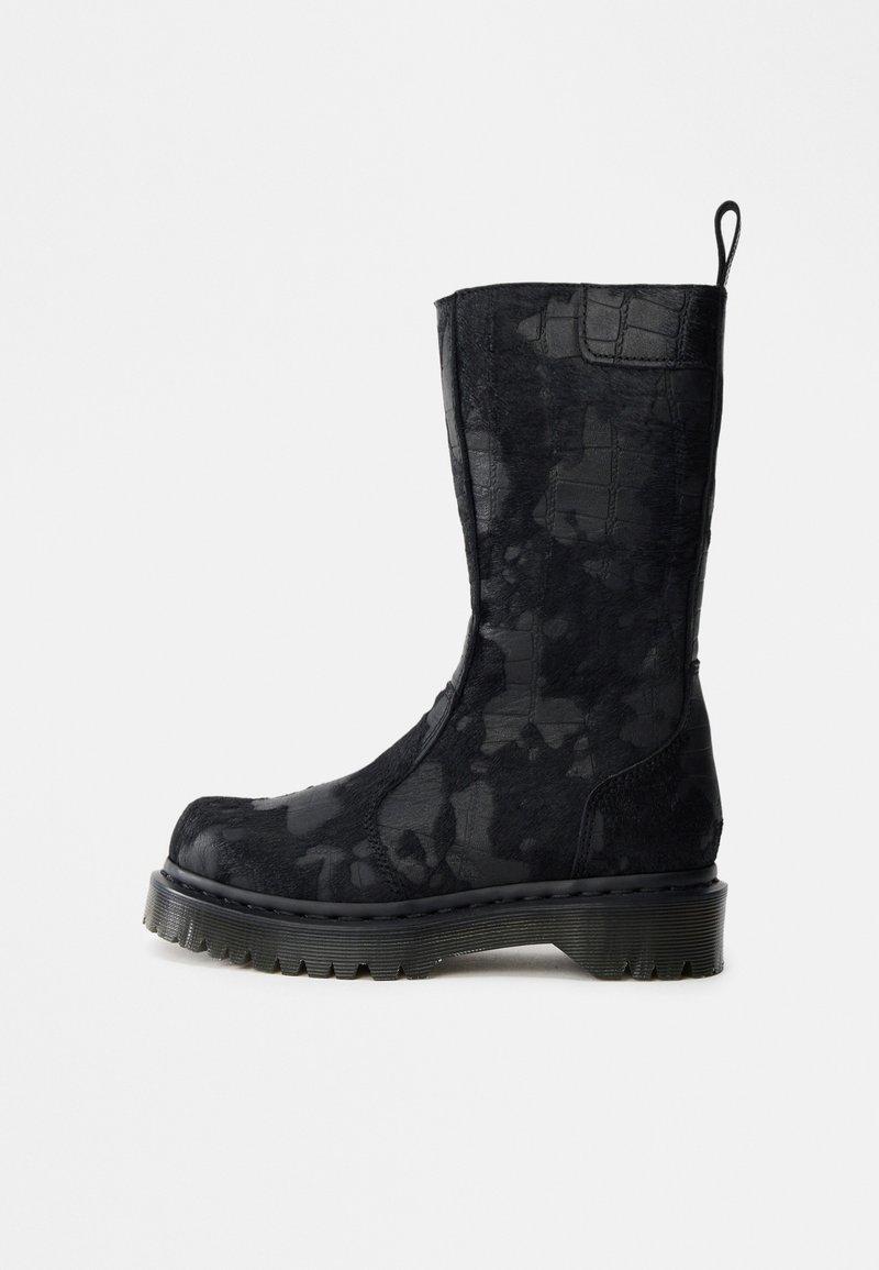 Stivale nero a metà polpaccio con motivo mimetico, suola spessa scanalata, punta arrotondata e linguetta posteriore, su sfondo bianco.